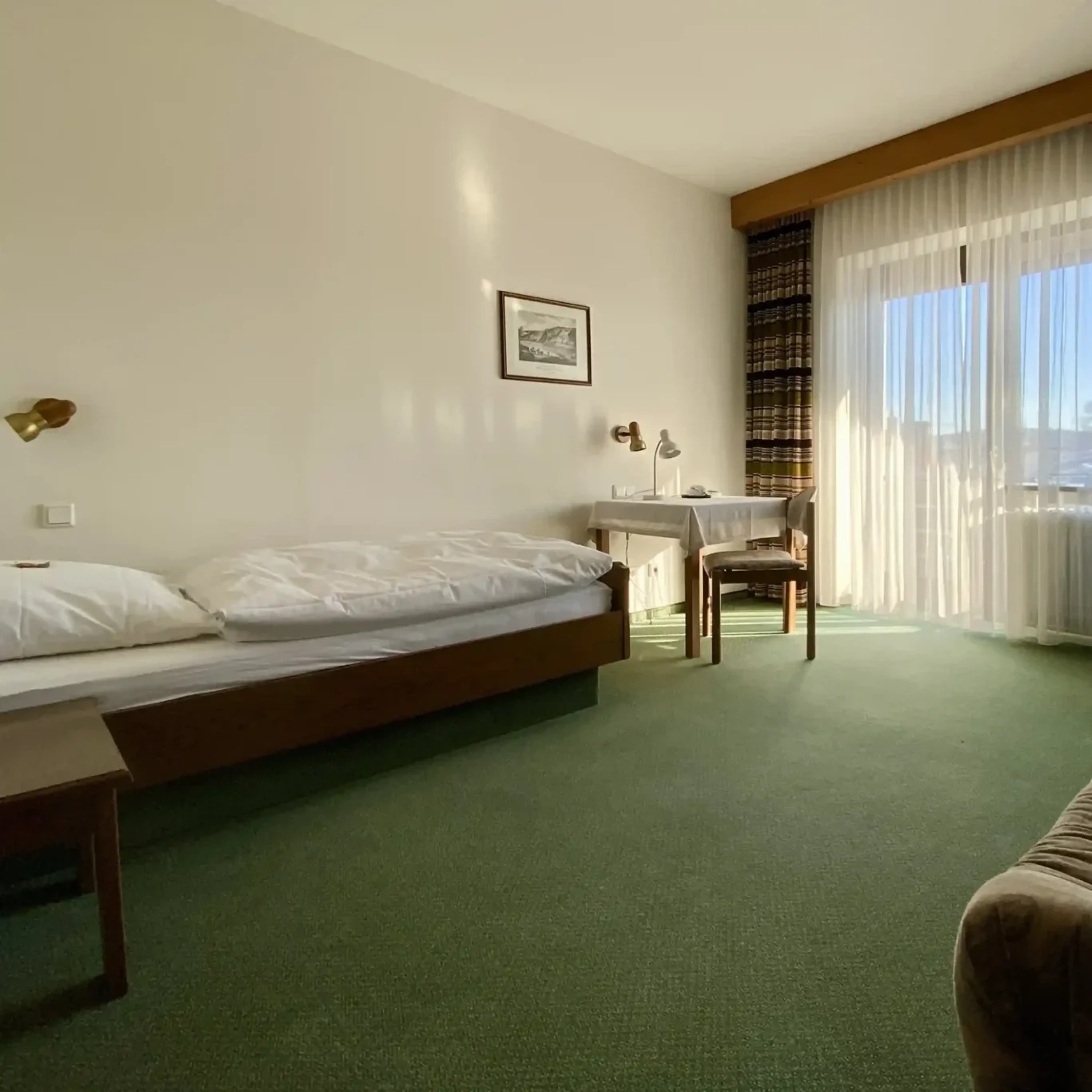 Hell eingerichtetes Doppelzimmer im Hotel Krieger mit Doppelbett, Sitzgelegenheit, TV und Zugang zum Balkon.