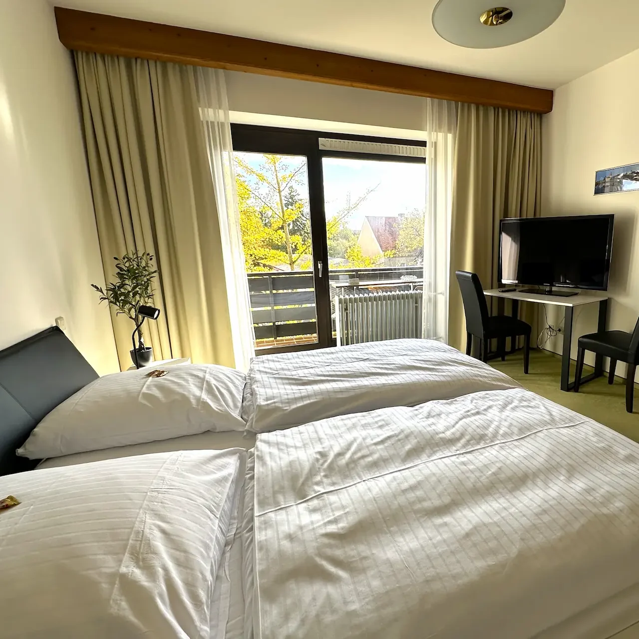 Komfort-Doppelzimmer mit Balkon – Entspannen in Mariaort. Hell eingerichtetes Doppelzimmer im Hotel Krieger mit Doppelbett, Sitzgelegenheit, TV und Zugang zum Balkon.