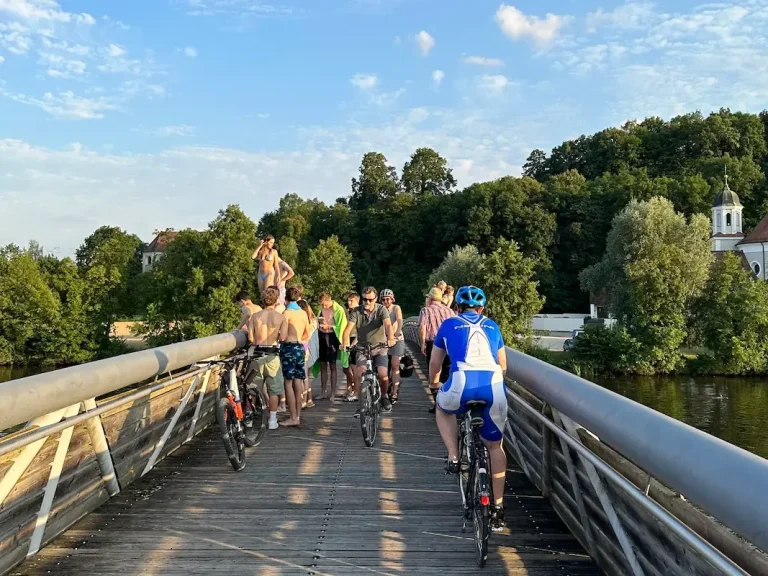 Radfahrer auf der Brücke und Badegäste beim Sprung in die Naab – Sommeridylle direkt am Hotel Krieger in Mariaort bei Regensburg.